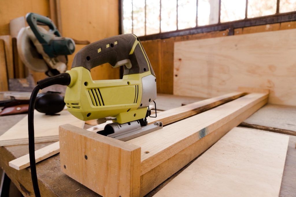 A close-up of an electric jigsaw placed on a wooden workbench in a carpentry workshop.